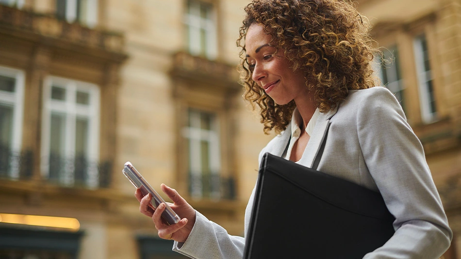 Donna manager che consulta il suo smartphone mentre si trova in giro, simbolo di mobilità e flessibilità del centralino virtuale TIM Ufficio Ovunque Sei