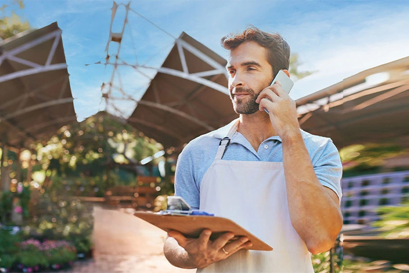 Uomo con cartellina da lavoro in mano risponde al telefono fisso dal suo smartphone grazie a TIM Ufficio Ovunque Sei
