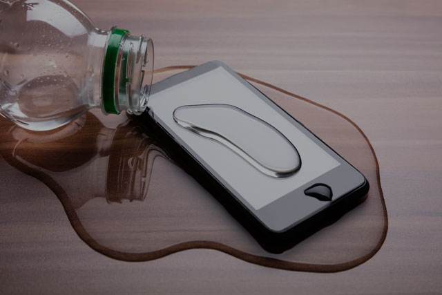 Smartphone con lo schermo rotto e liquido versato accanto, simbolo di danno accidentale.