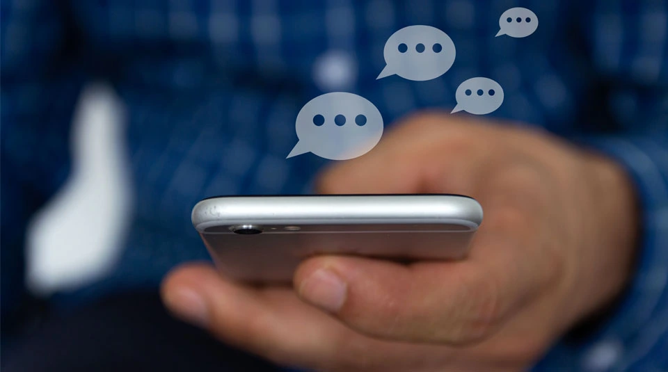 Mano maschile regge uno smartphone con icone a forma di nuvoletta a indicare l'invio di messaggi