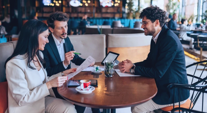 Persone sedute al tavolo di un bar discutono di lavoro e navigano gratis su internet grazie alla soluzione wi-fi per aziende di TIM