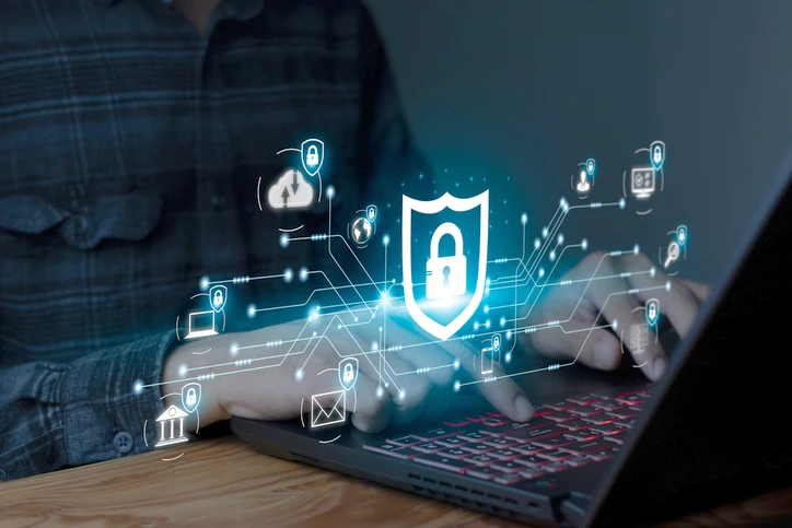 Mani che scrivono su un laptop, in sovrimpressione diverse icone che vanno a formare una rete sicura e protetta secondo la NIS2