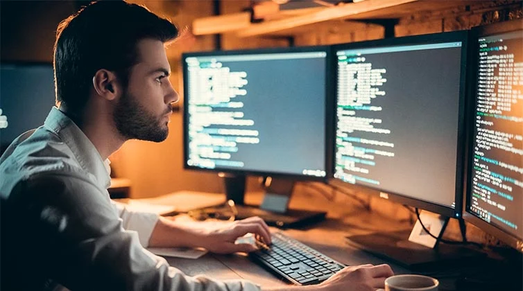 Uomo seduto davanti a diversi schermi di computer mentre gestisce un incidente informatico e fornisce assistenza al cliente sotto attacco dei cyber criminali