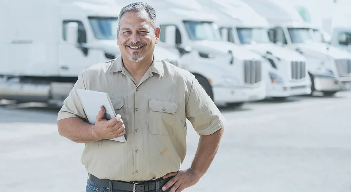 Professionista sorridente con tablet in mano, davanti a una flotta di camion bianchi, a indicare la gestione efficiente della flotta aziendale con soluzioni di geolocalizzazione avanzate